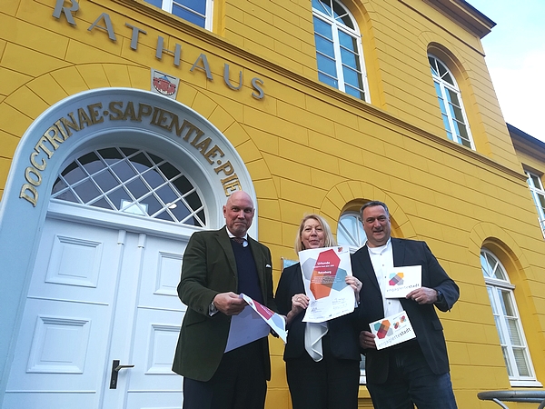 Das Bild zeigt Stadtpräsident Andreas von Gropper, Regionalvorständin Kerstin Andresen von der Volksbank Raiffeisenbank eG und Bürgermeister Eckhard Graf vor der Tür des Ratzeburger Rathauses. Sie präsentieren das Logo "Engagierte Stadt"