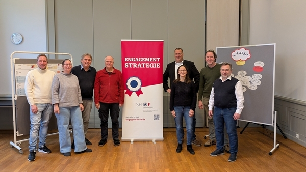 Das Bild zeigt die achtköpfige Steuerungsgruppe der geplanten Engagementstrategie für die Stadt Ratzeburg im Ratssaal des Ratzeburger Rathauses in einer Gruppenaufnahme vor einem Banner mit der Aufschrift "Engagementstrategie".